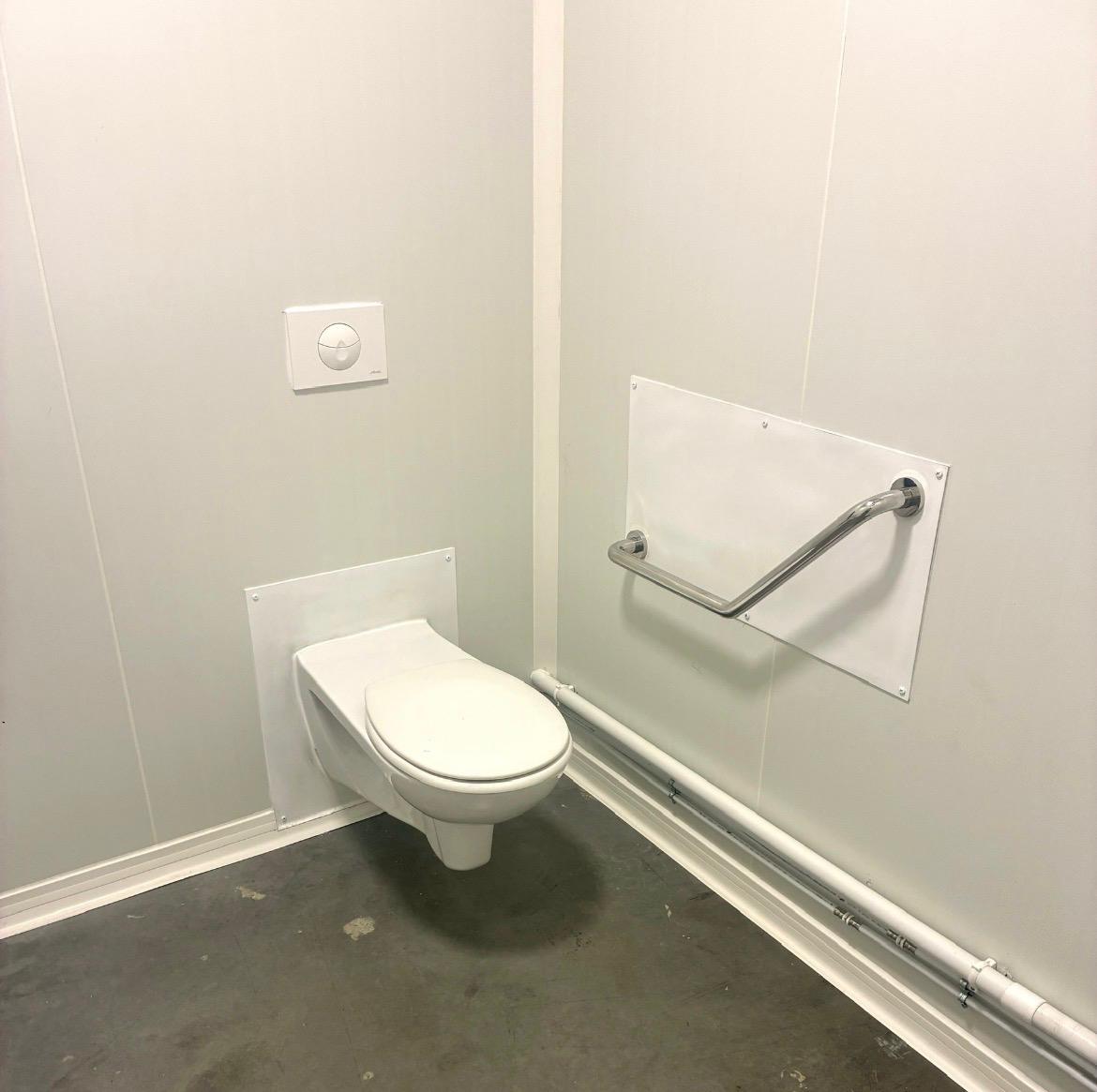 WC suspendu et barre d'appui fixés sur plaques acier dans un local sanitaire